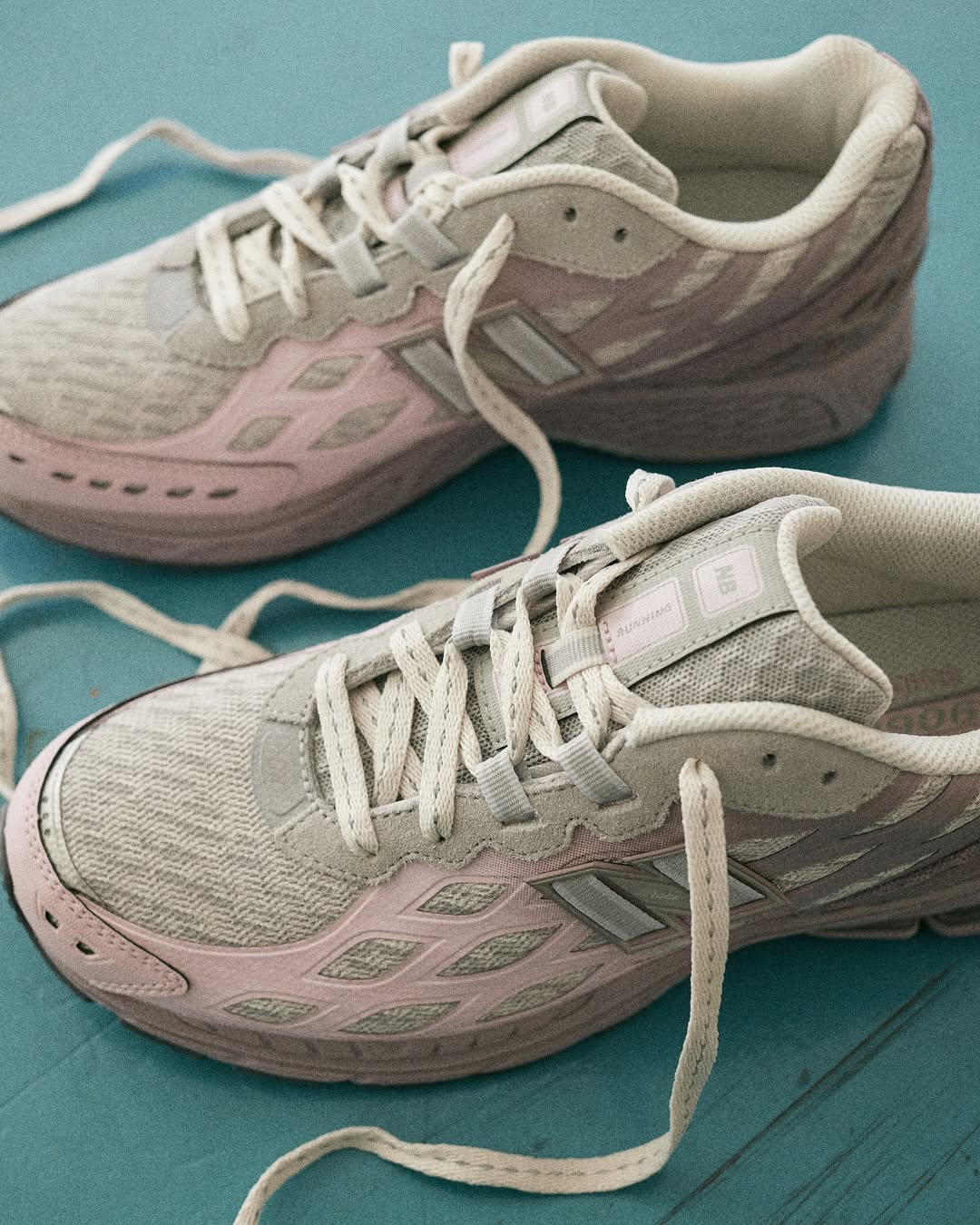 New Balance 1906W women’s trainers in Ice Wine and Mid Century Pink with mesh and suede details on teal floor.