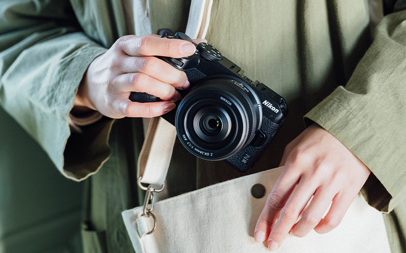 Close-up view of a person holding the Nikon Z30 travel camera with the NIKKOR Z DX 24mm f/1.7 Lens.