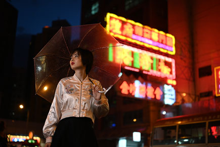 An Asian woman holding an umbrella with a backdrop of night city lights