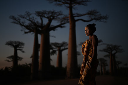 A woman in traditional dress standing against a backdrop of baobab trees