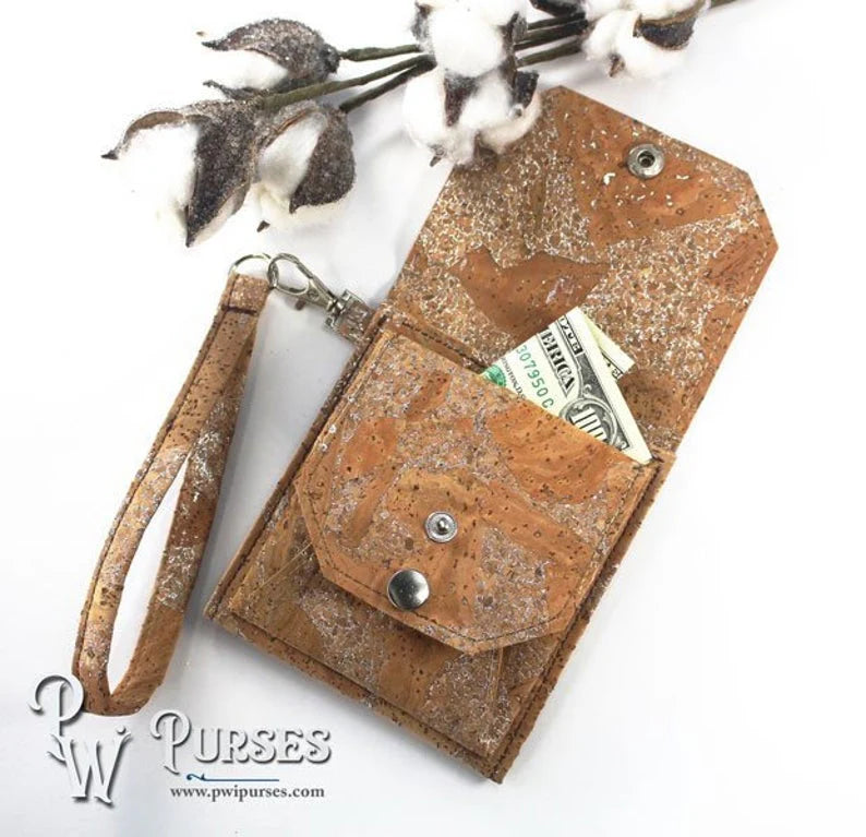 A cork wristlet wallet with an open pocket containing cash next to white cotton branches.