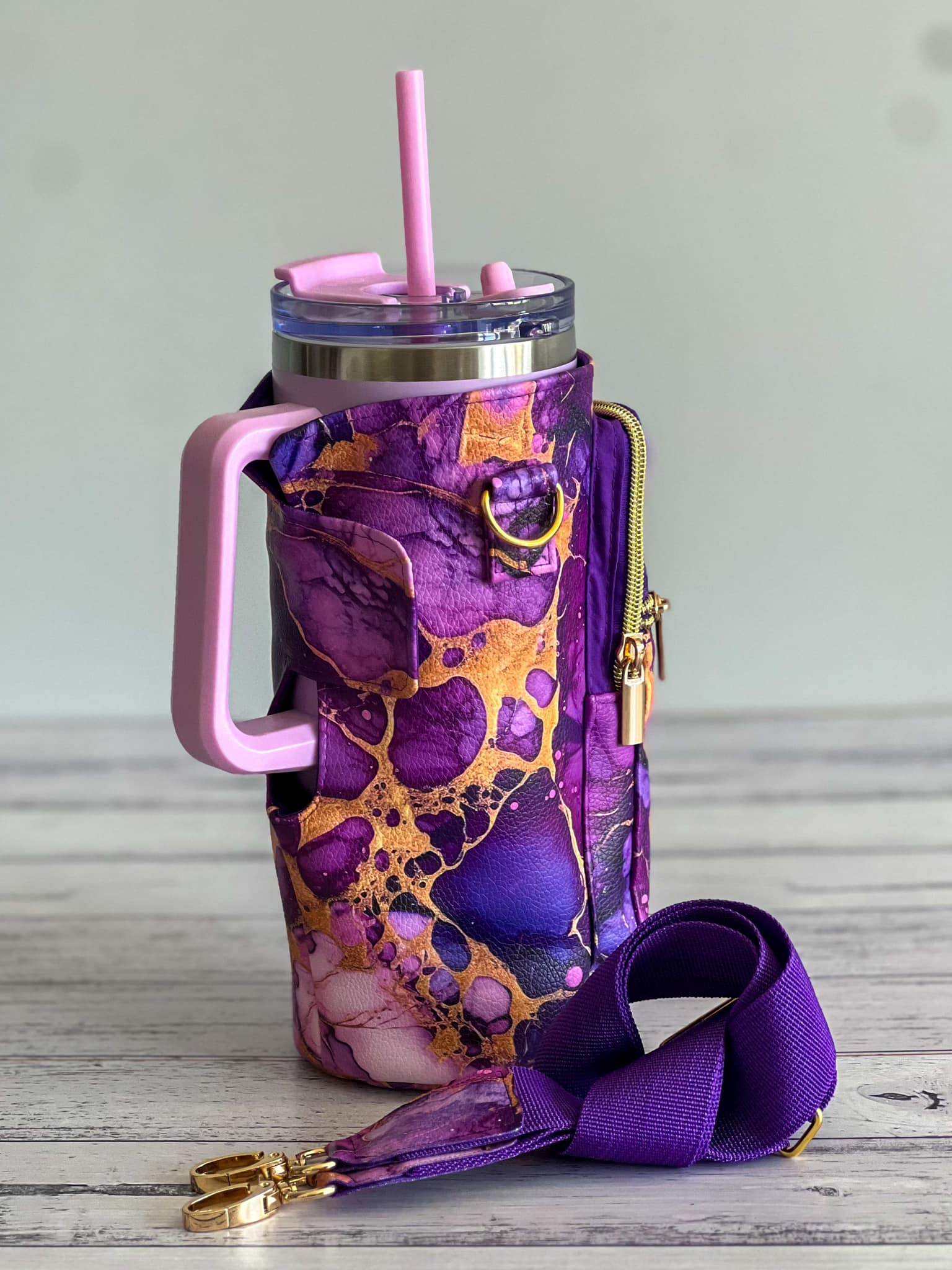 Purple and gold marble insulated tumbler with pink handle and straw, and matching detachable strap.