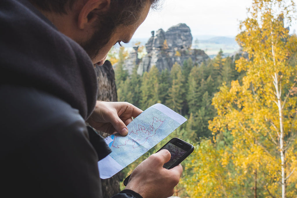 A person checking a paper map and a camping app