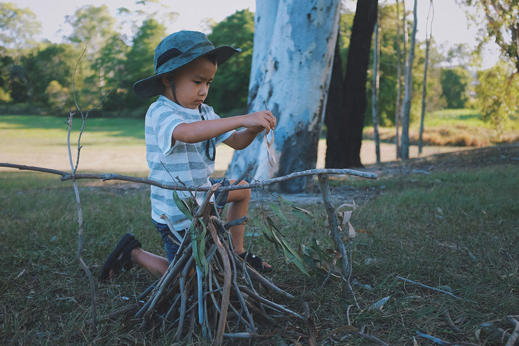 A boy in a sun hat building a campfire