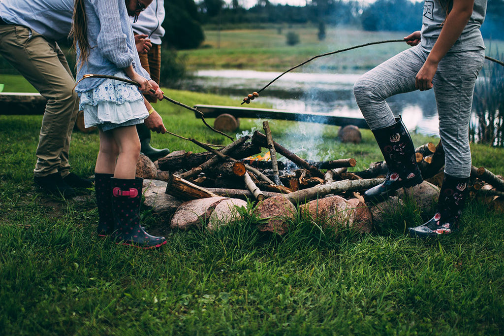 Adults and kids grilling food over a campfire