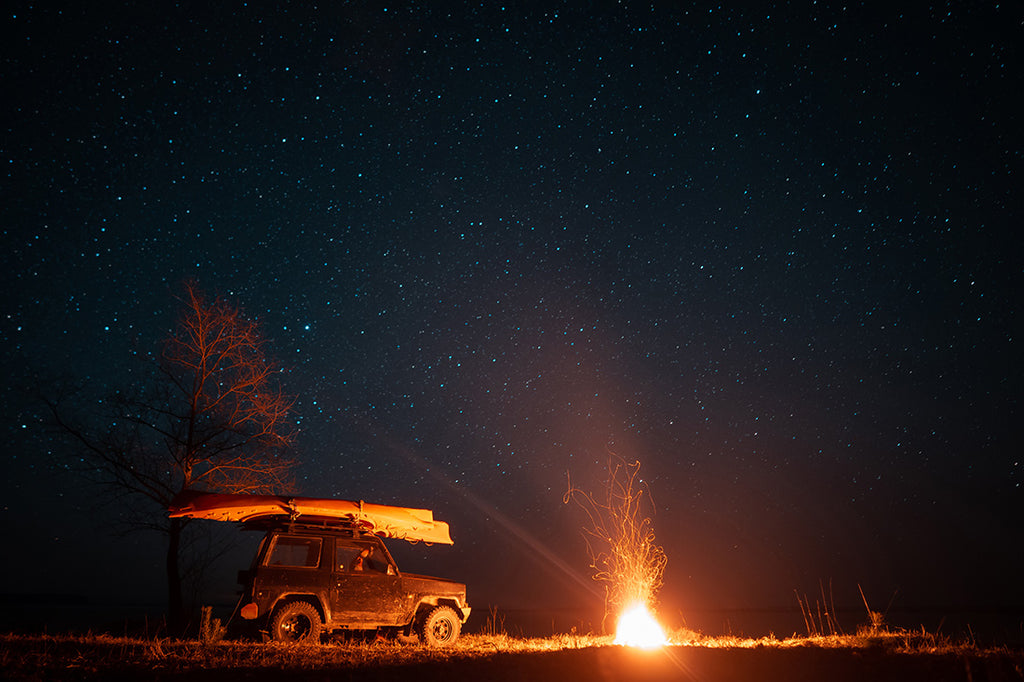 A car at night parked near a campfire