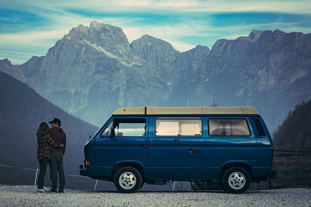 Two people in the mountains standing next to a blue campervan