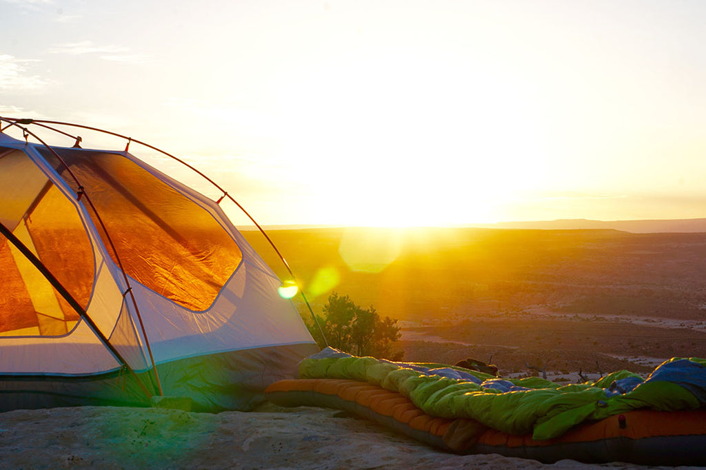 Tent and sleeping bag on a cliff at sunrise