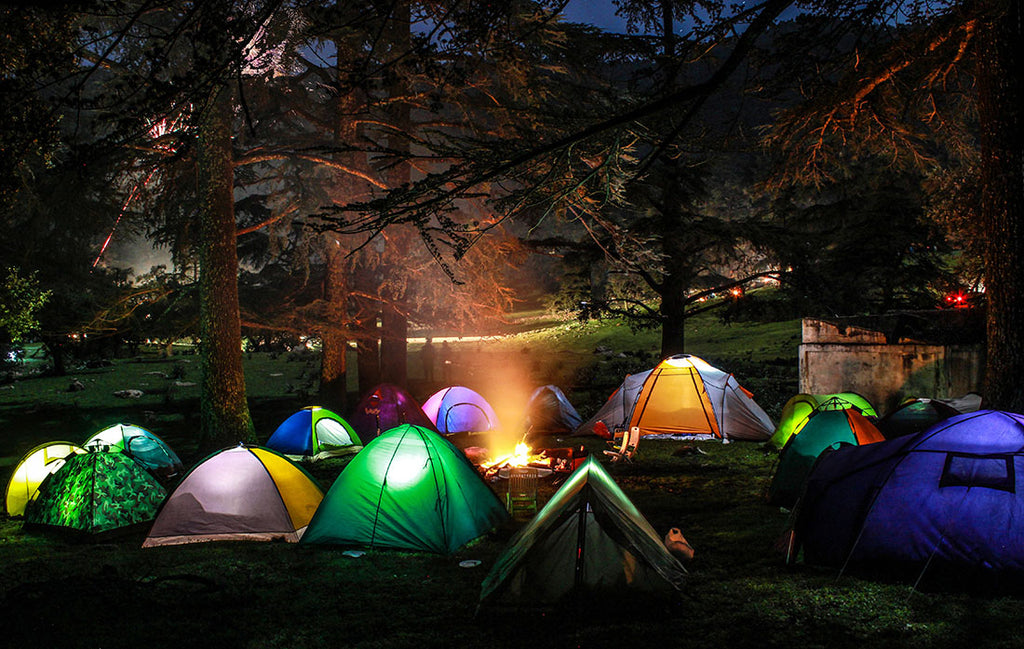 Multiple colored tents surrounding a campfire at night