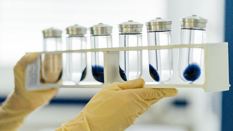 Gloved hands holding a rack of vials containing blue samples suspended in liquid