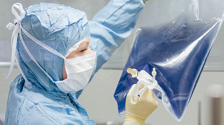 Doxtor in full lab gear examininga bag of blue liquid