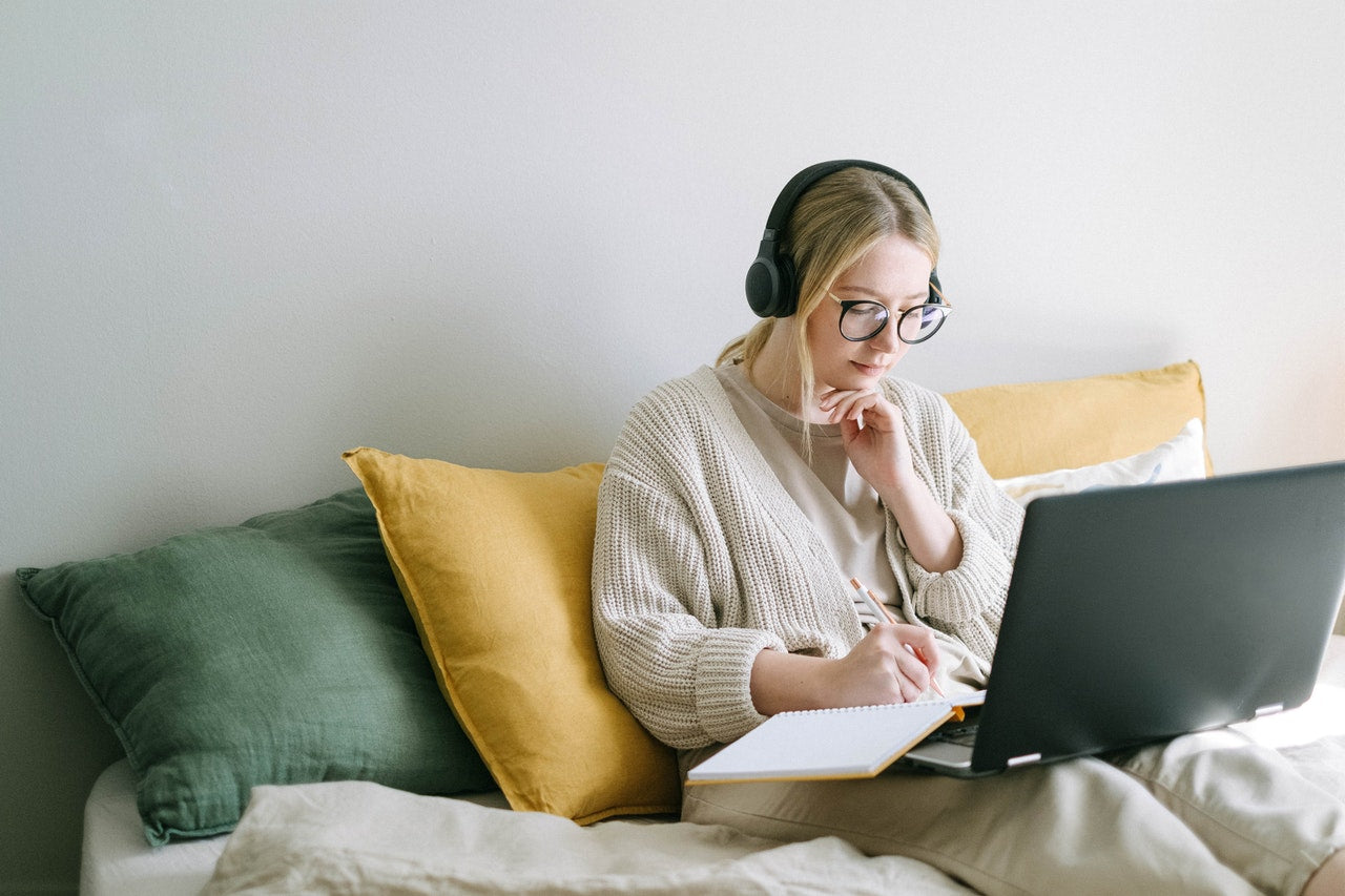 Image of a woman sitting on her couch with a laptop and notebook working on developing a SaaS content marketing strategy