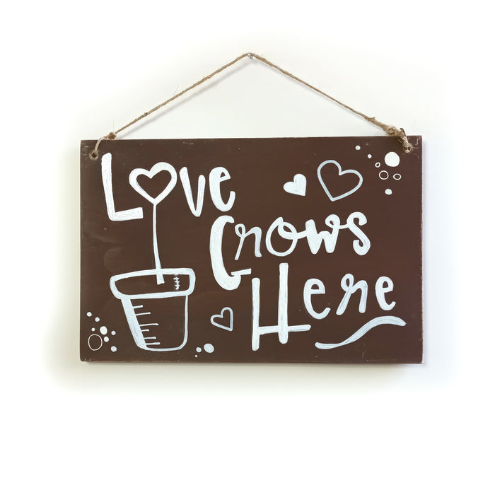 Letrero de madera con frase “LOVE GROWS HERE".