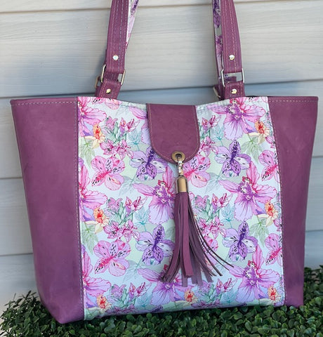a tote bag, with pink leather side accents ona floral pink fabric, finished off with a silver tassel.