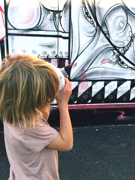 boy using a white camera to take a photos of graffiti art on a warehouse