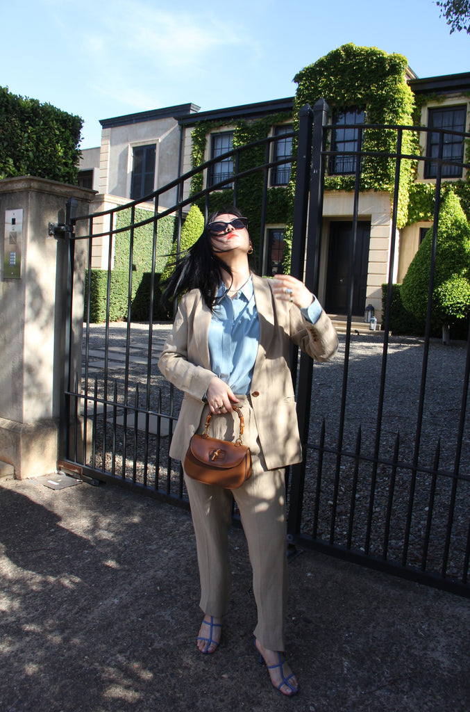 Petite fashion influencer wearing taupe linen blazer and trouser, blue button-up shirt, blue heels and brown leather handbag