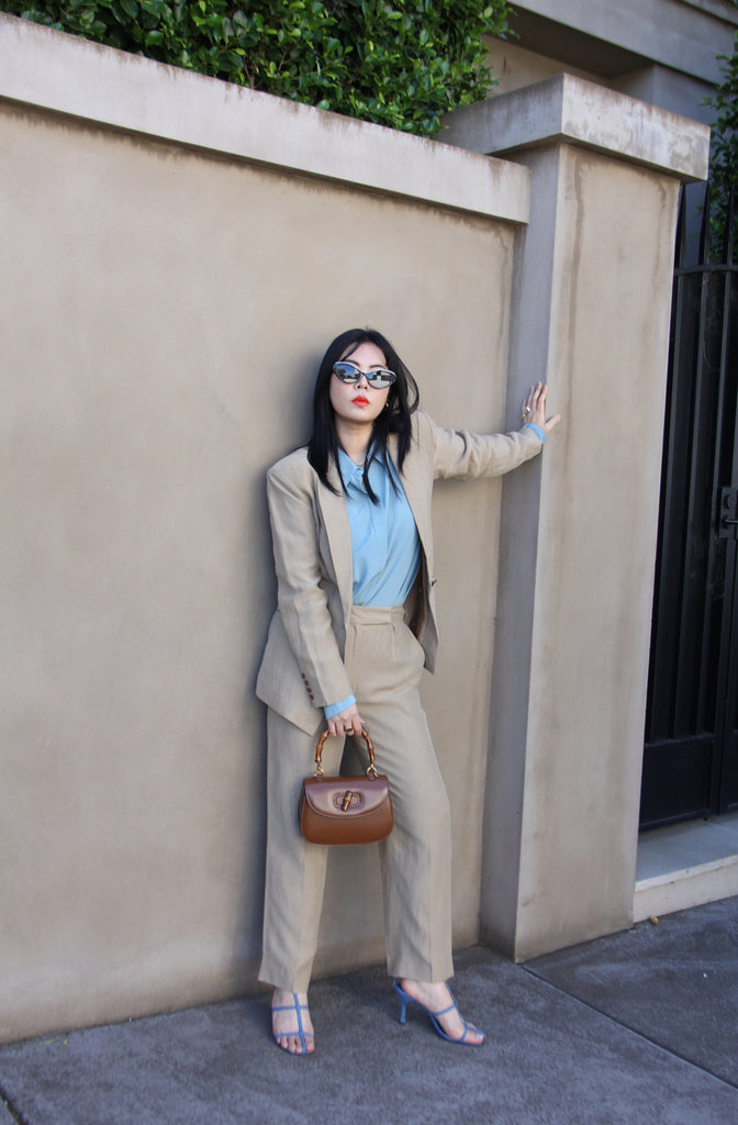 Petite fashion influencer wearing taupe linen suit, blue button-up shirt and blue sandals.