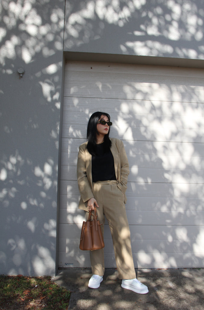 Petite fashion influencer wearing taupe linen blazer and pant, black t-shirt and white sneakers