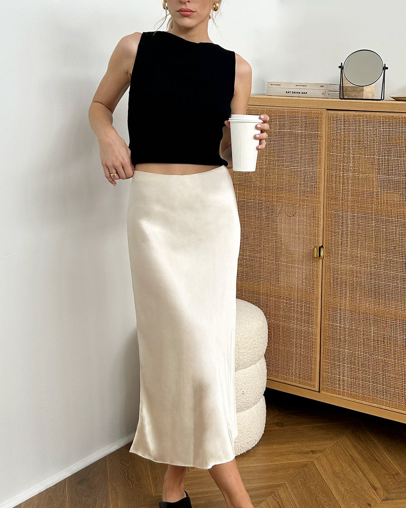 Woman wearing black tank top and cream silk slip skirt posing with a coffee