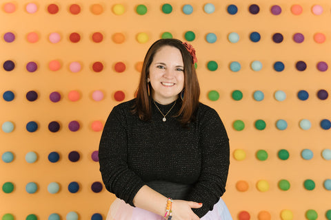 Etsy coach Nicole Lewis is pictured in a black shirt on an orange background that has rainbow balls.