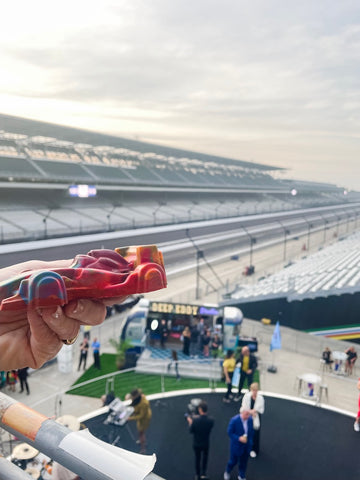 Hand holding out a red colored car crayon from high above, over looking the track at the Indianapolis Motor Speedway
