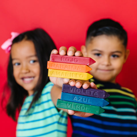 Two children holding Spanish Crayon Stix sets from Art 2 the Extreme in 9 solid colors. Give them as school gifts for the start of school year or to create homemade Mother's Day cards.