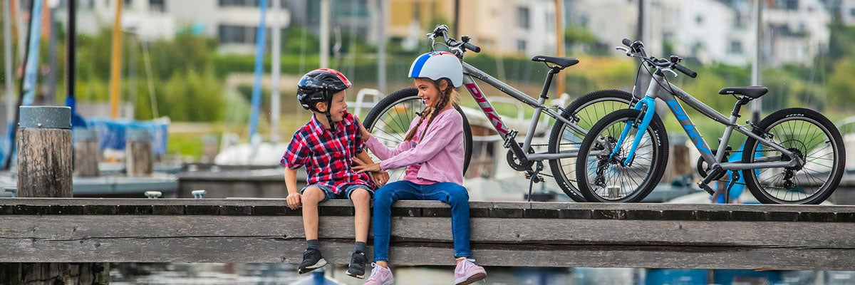 Zwei Kinder mit Fahrradhelm und ihren Fahrrädern sitzen am Hafen