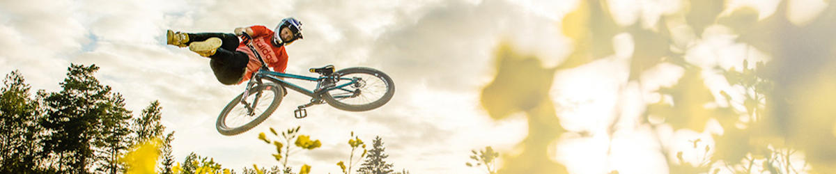 Junger Mann springt mit einem MTB und MTB-Reifen über einen Hügel