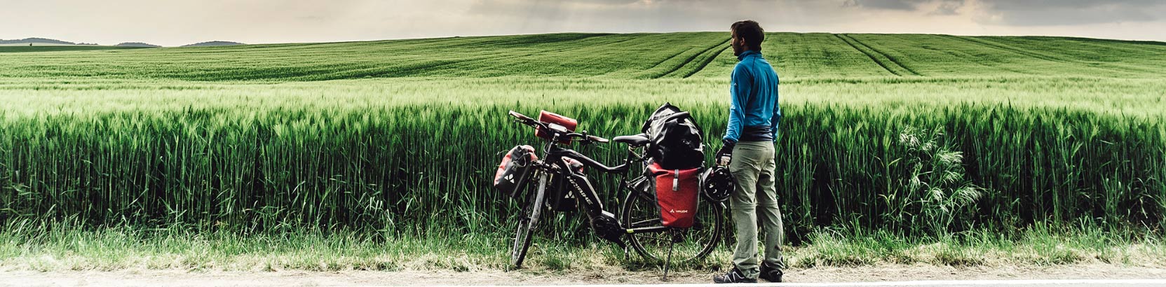 Mann mit Packtasche auf einem Trekkingbike vor einem Feld