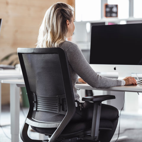 Frau sitzt auf einem ergonomischen Bürostuhl mit Lordosenstütze.