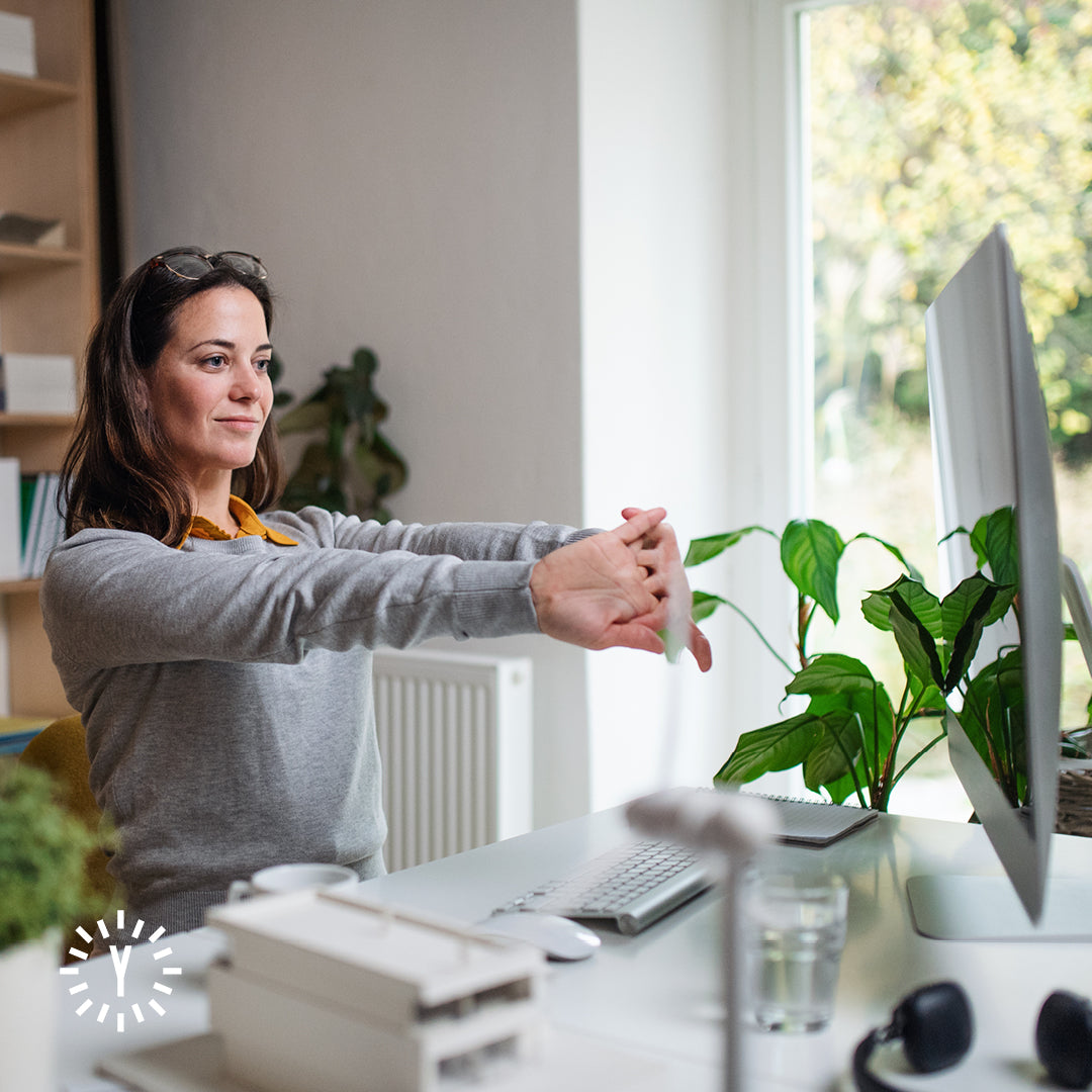 Frau dehnt sich im Stehen an einem höhenverstellbaren Tisch im Homeoffice.