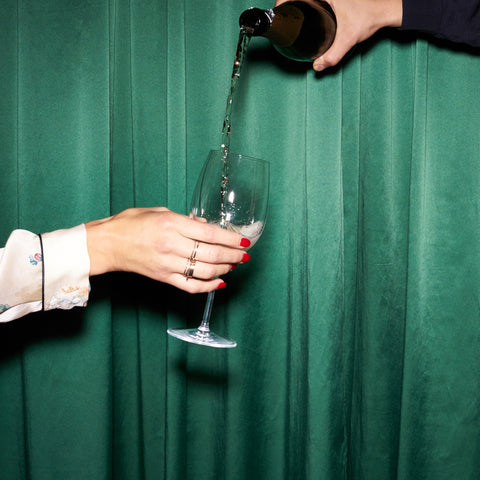 champagne being poured into a glass with a hand holding it against a green backdrop.