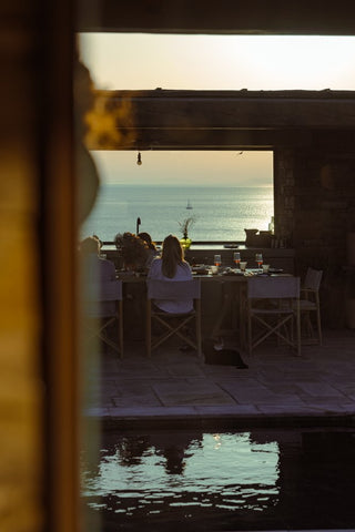 people sitting at an outdoor dining table with the ocean in the background