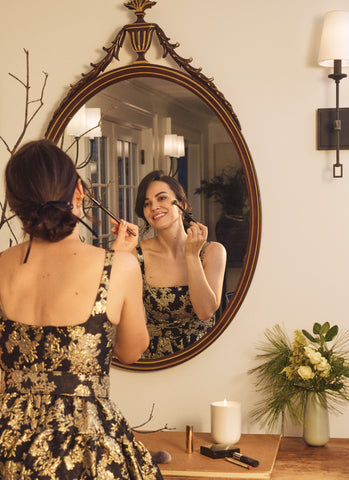 woman looking in a mirror putting makeup on