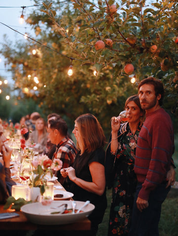 a man and a woman standing next to a set table in an apple orchard