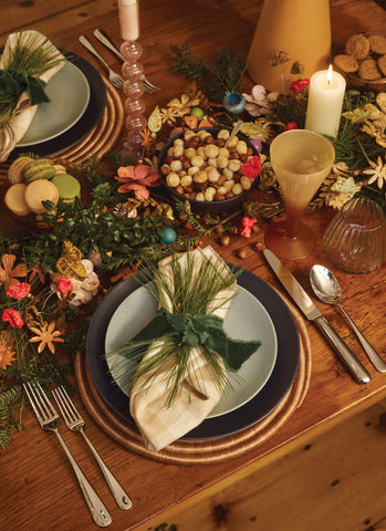 a table set for the holidays with ceramic plates, a napkin, and festive candles and decoration down the center