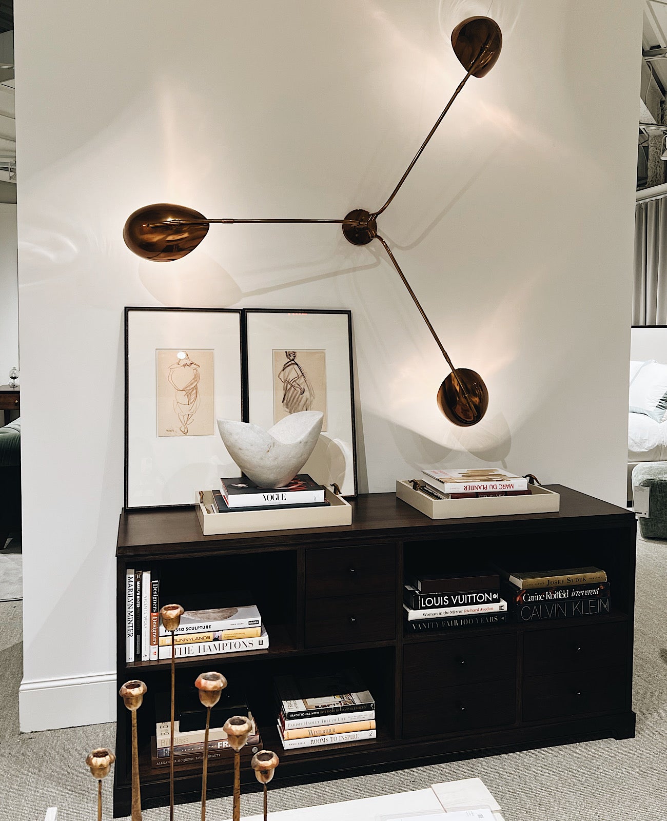 A wall unit display of home decor and coffee table books, above the display are two framed prints and an architectural lightform that has been displayed on the wall as an additional work of art.