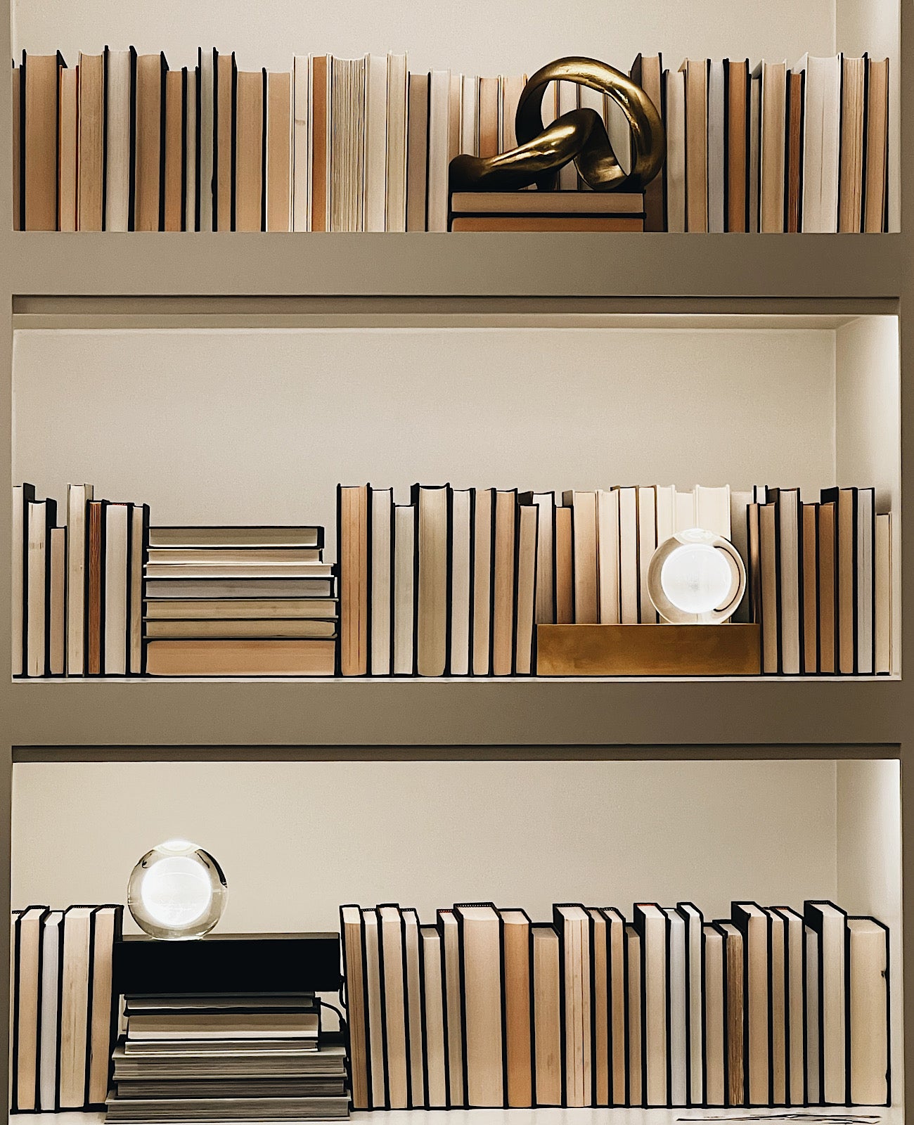 A bookcase filled with neutral toned books and accents of portable lights.