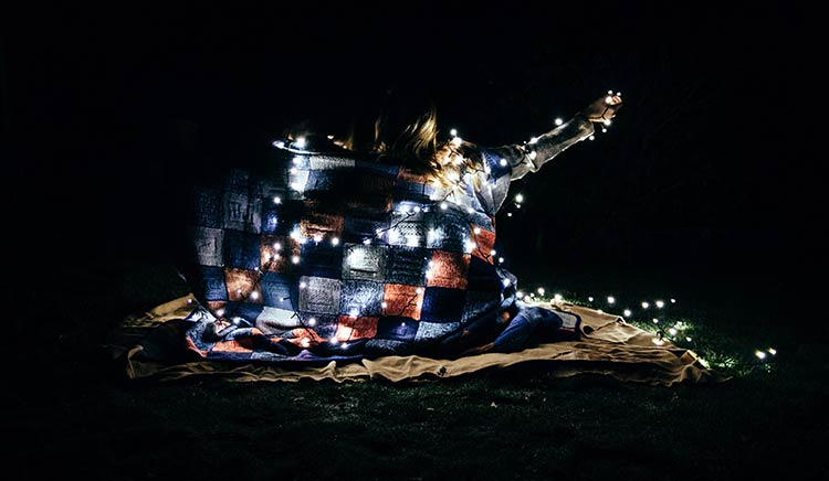 A couple wrapped in a blanket, surrounded by fairy lights