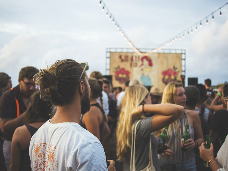 A man with his hair in a bun, looking out at a festival. 