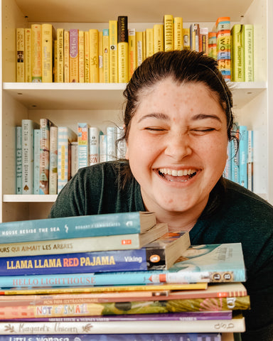 ashley in front of a bookshelf holding a stack of childrens books and laughing out loud