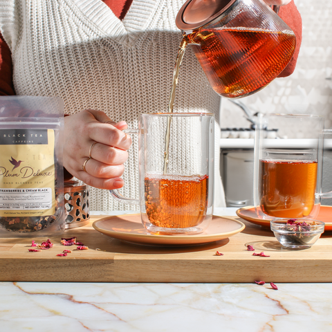 person pouring loose leaf tea, brewed, into a glass mug