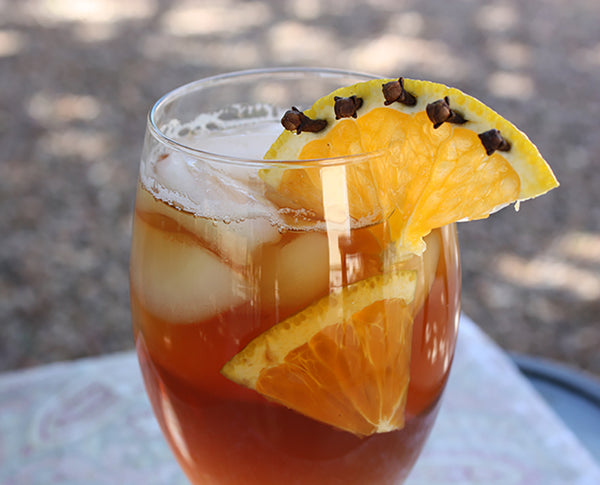 A glass of iced tea is garnished with clove-studded orange slices.