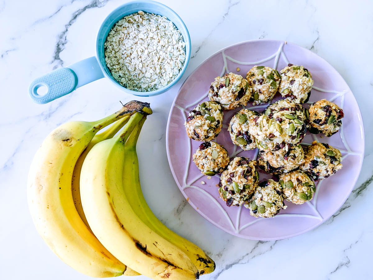 A plate of banana energy bites alongside a cup of oats and a bunch of bananas.