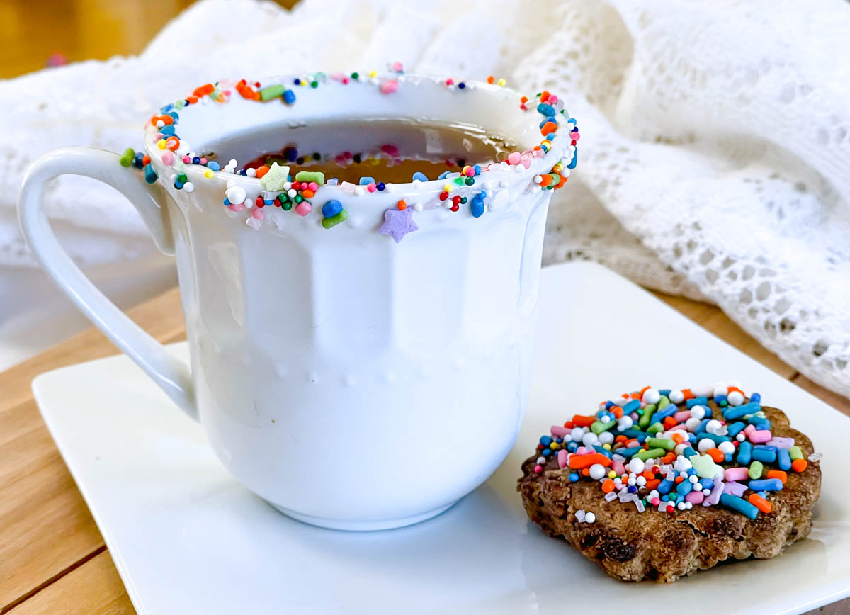 Teacup with a colorful rim of sprinkles and an accompanying cookie.