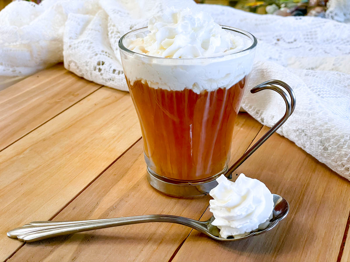 Cup of tea with a dollop of whipped cream on top, in the process of melting in.