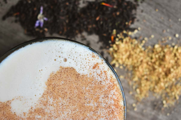 Overhead view of a black tea latte surrounded by sprinkles of ginger and tea leaves.