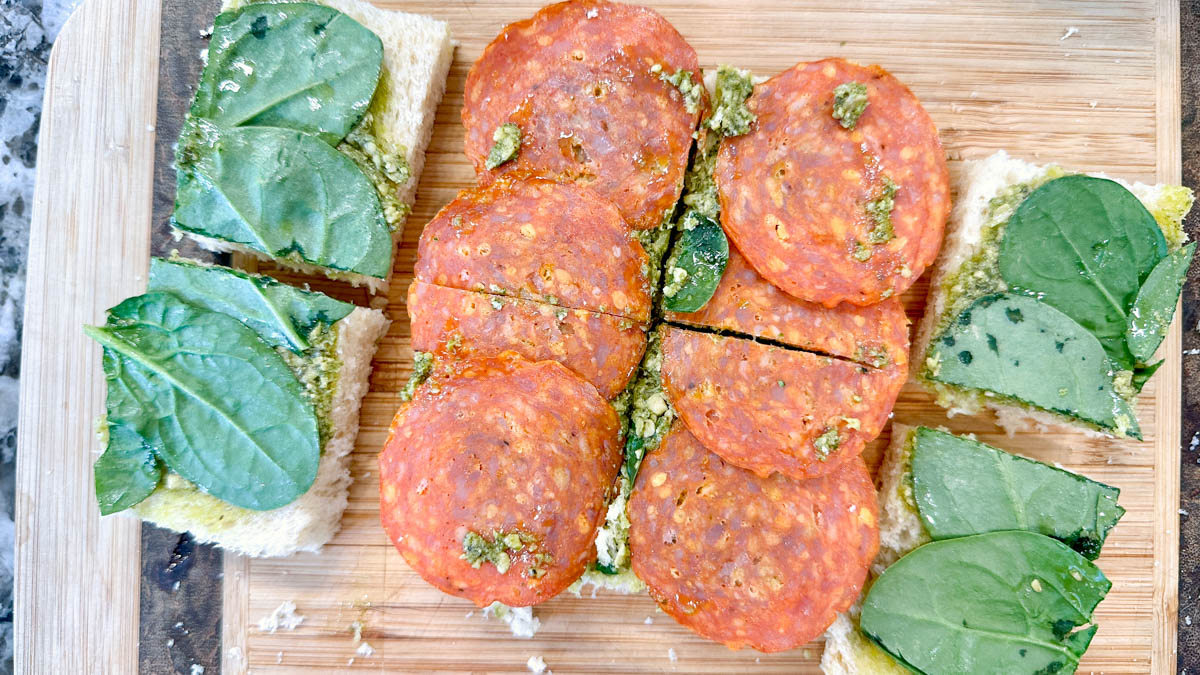Cut open sandwiches with pesto, pepperoni and spinach, waiting for the burrata cheese.