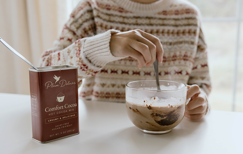 Photo of a person in a brown and white nordic knit sweater stirring a large glass mug of Plum Deluxe Comfort Cocoa.