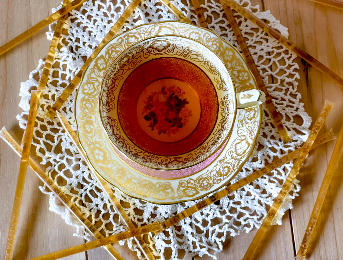 A cup of black tea on a tea cozy surrounded by an artistic lattice of honey sticks.